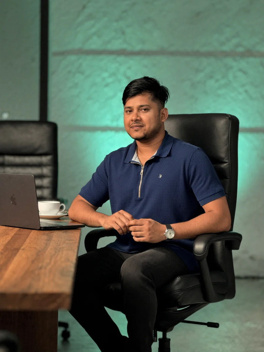 Raisul at a desk with a laptop and a cup of coffee, looking towards the camera.